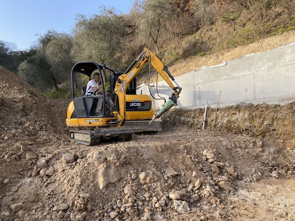 un operaio manovra un piccolo escavatore in un campo sterrato.
