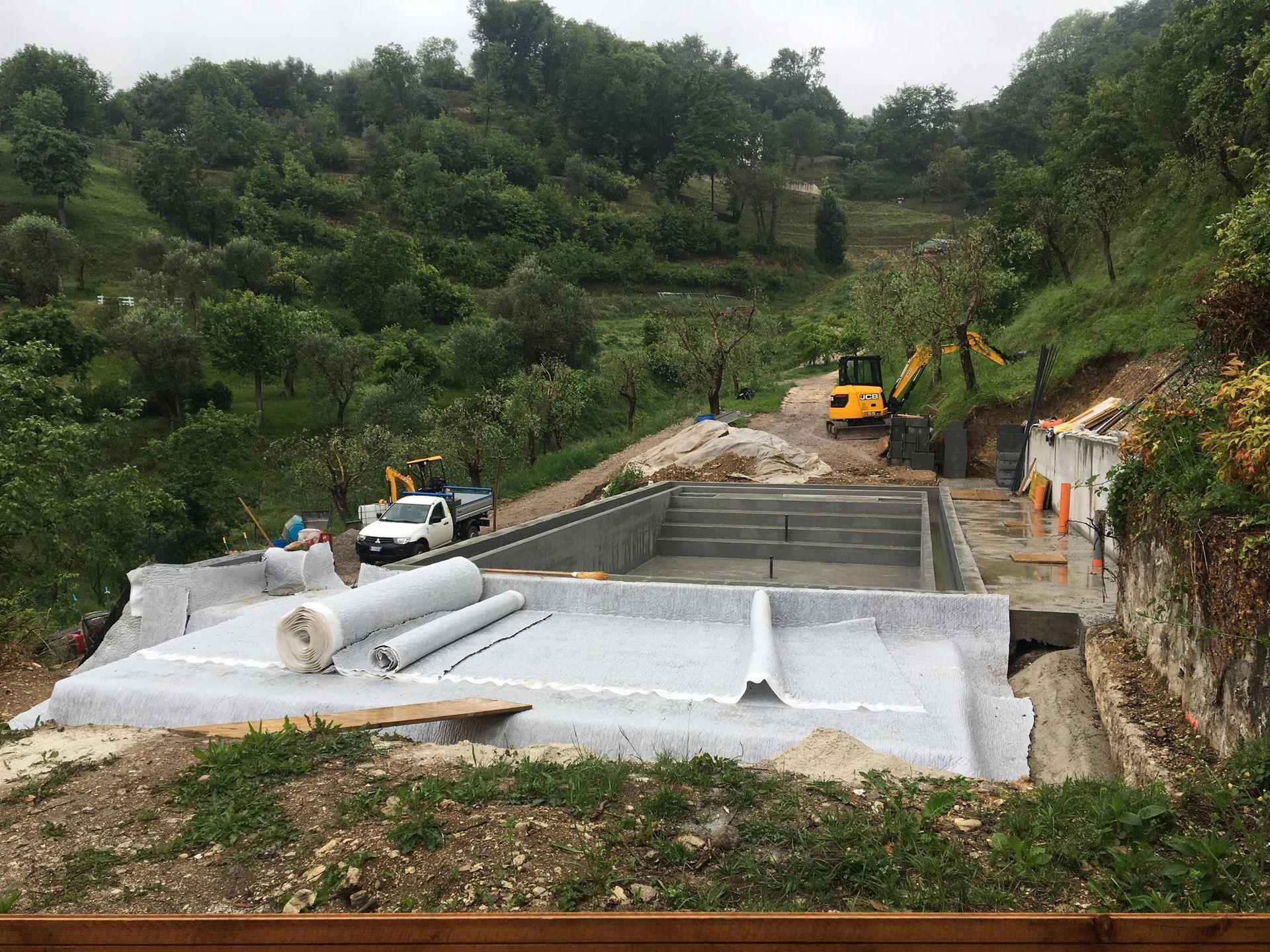 Un cantiere con un escavatore giallo sullo sfondo. Realizzazione Piscina