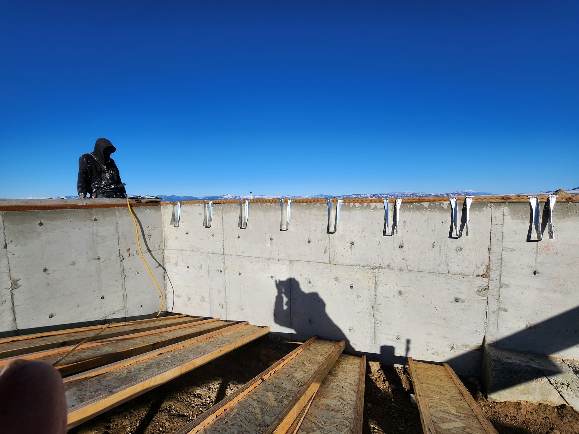 A person is standing on a wooden deck next to a concrete wall.