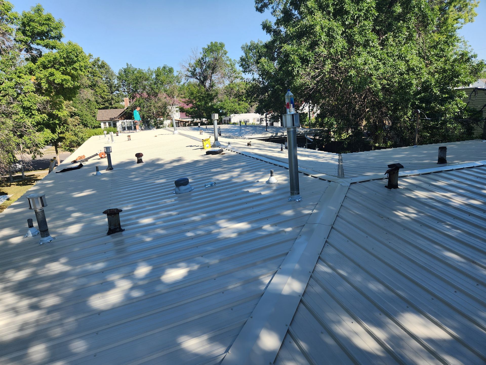 The roof of a house with a metal roof and trees in the background.