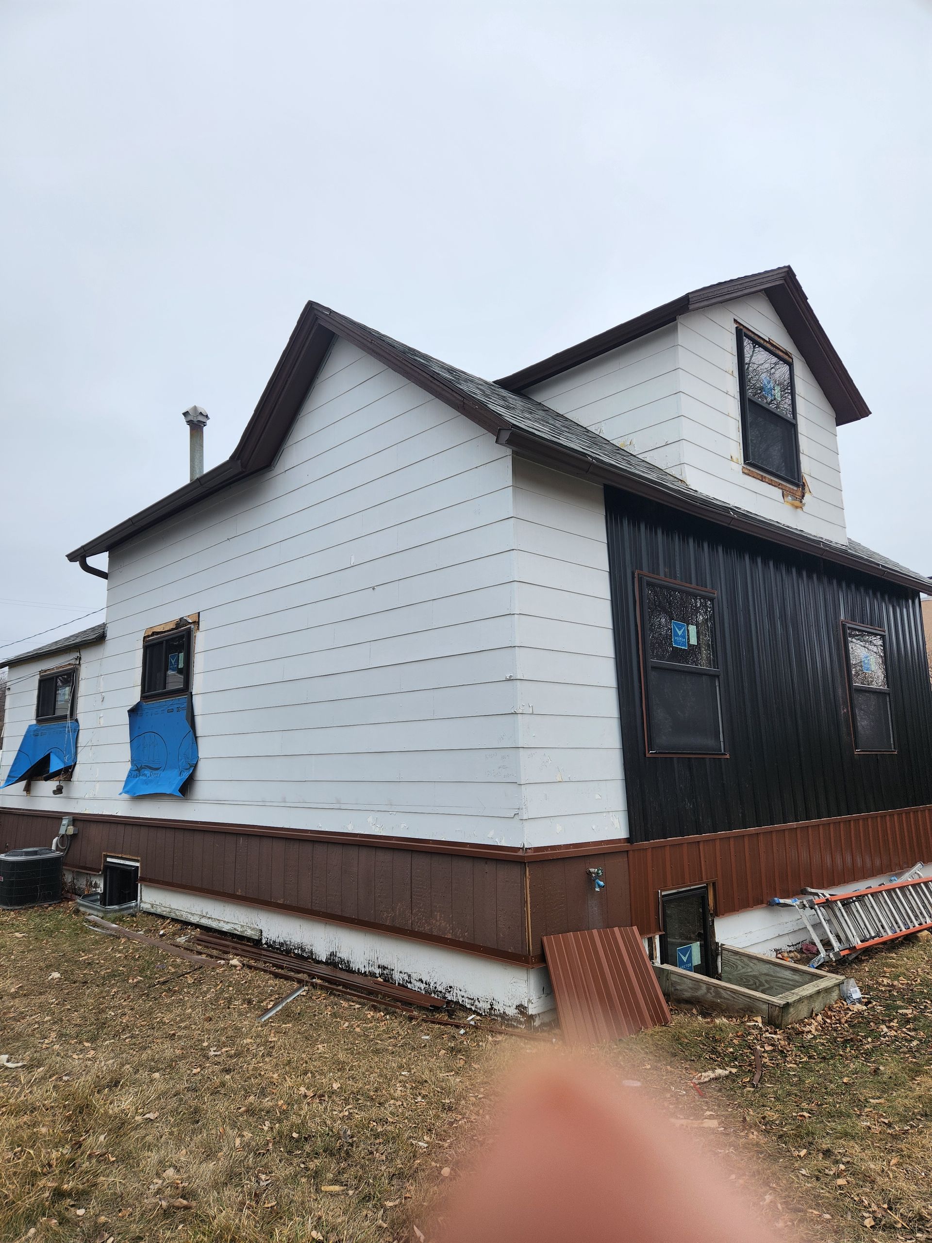 A white house with a black roof is being remodeled.