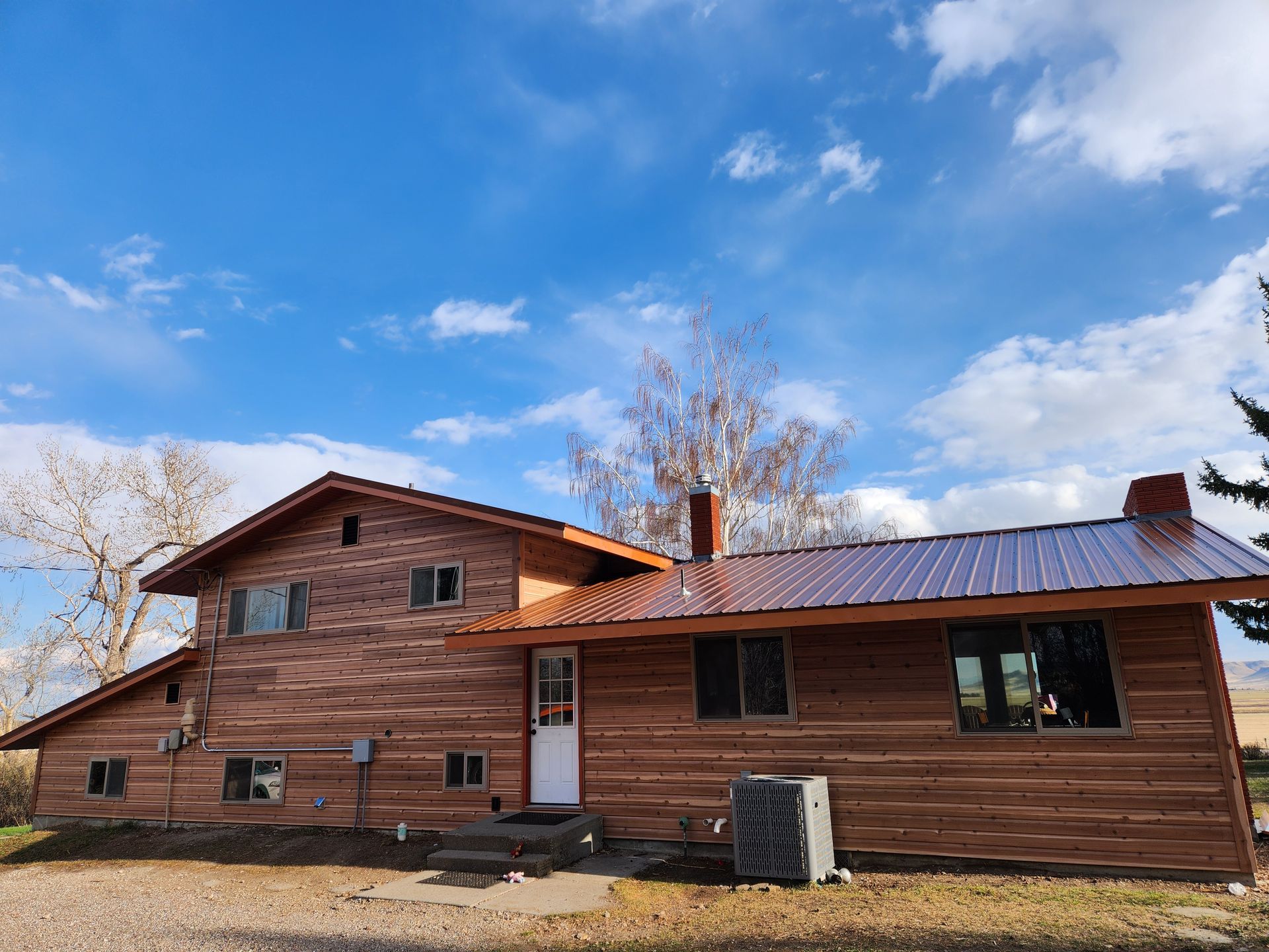 A large log cabin with a metal roof is sitting on top of a dirt field.