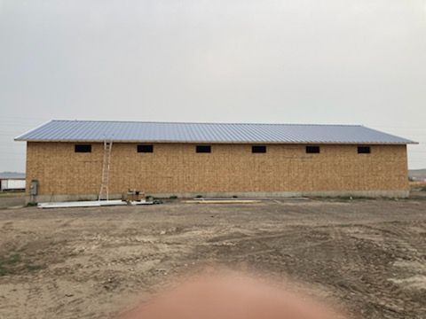 A large wooden building with a metal roof is being built in a dirt field.