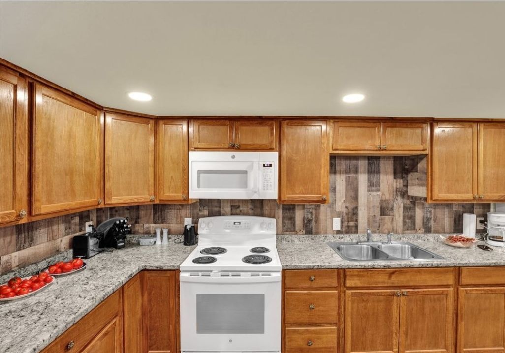 A kitchen with wooden cabinets , granite counter tops , a stove , microwave and sink.