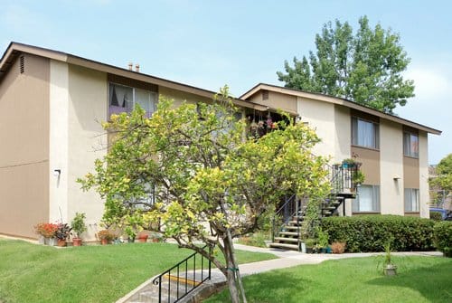 Exterior of a two story apartment building with green grass outside, trees, and a sidewalk.