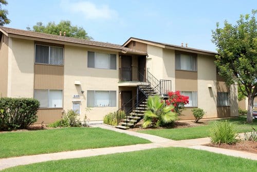 Exterior of a two story apartment building with green grass outside and a sidewalk.