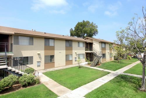 Exterior of a two story apartment building with green grass outside and a sidewalk.