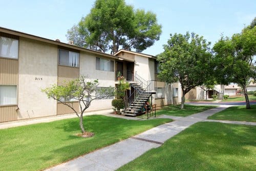 Exterior of a two story apartment building with green grass outside and a sidewalk.