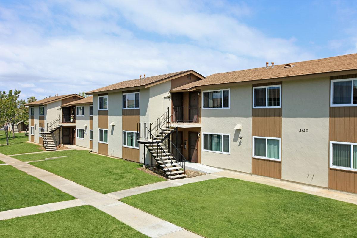 Exterior of a two story apartment building with green grass outside and a sidewalk.