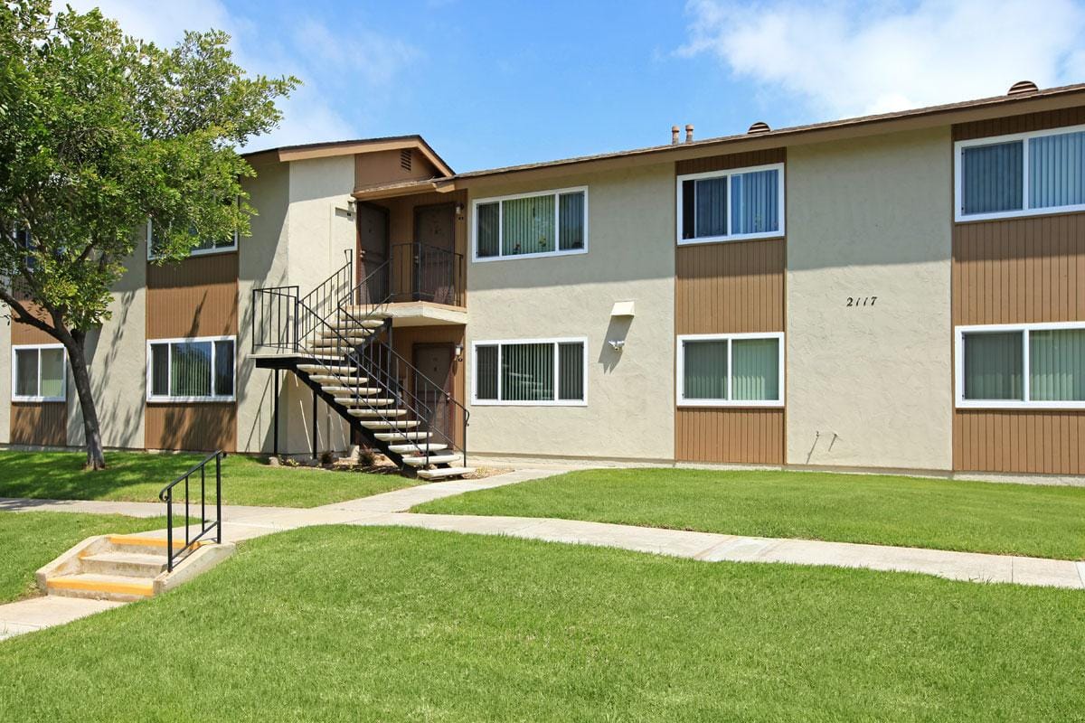 Exterior of a two story apartment building with green grass outside and a sidewalk.