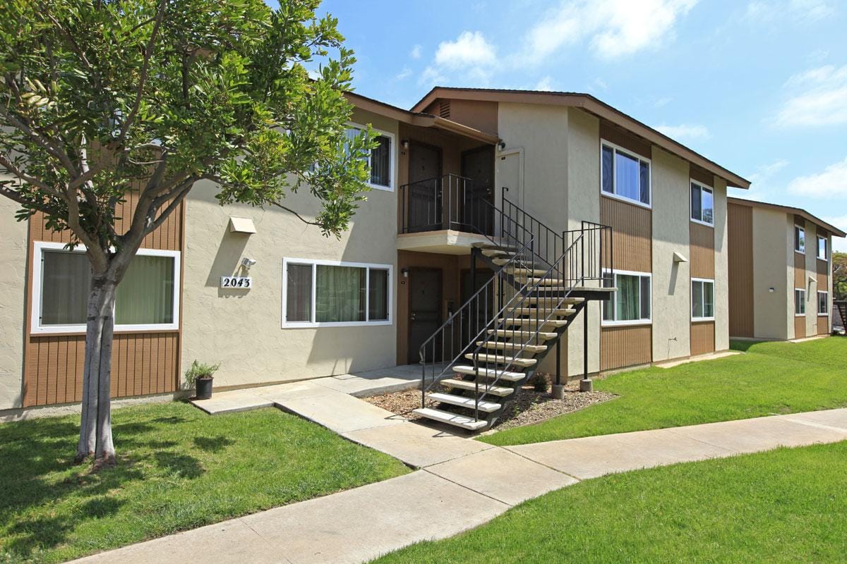 Exterior of a two story apartment building with green grass outside and a sidewalk.