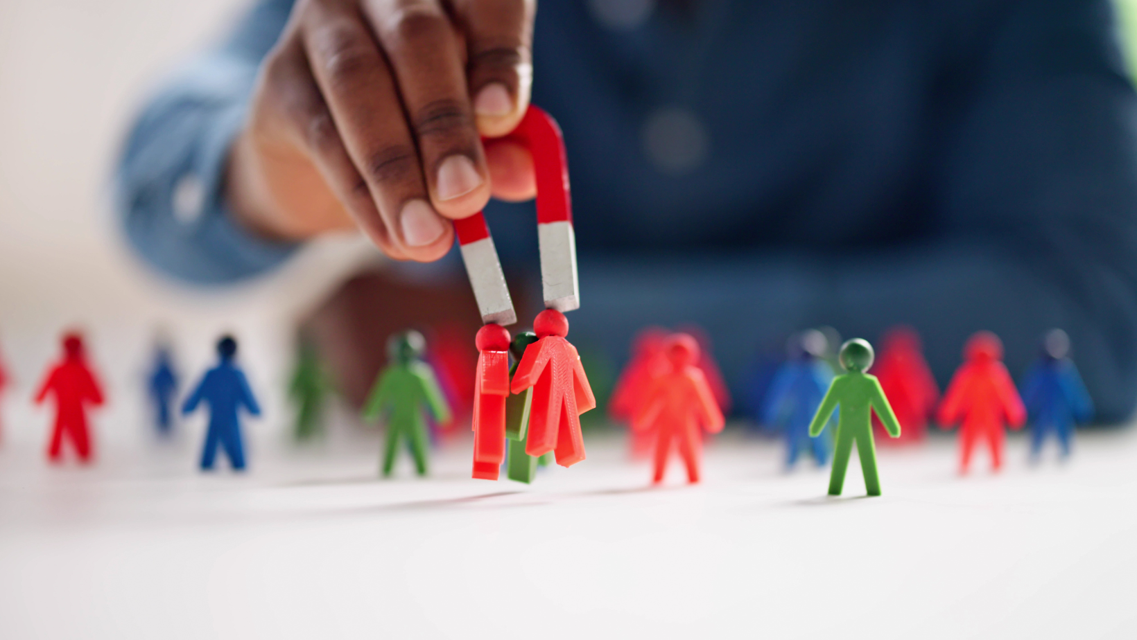 A person is holding a magnet over a group of magnetic people.