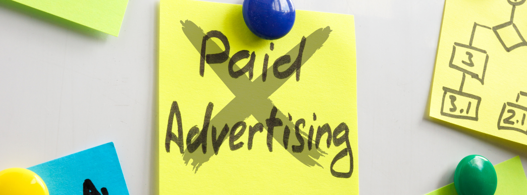 A yellow sticky note with crossed out words that say paid advertising is pinned to a whiteboard.