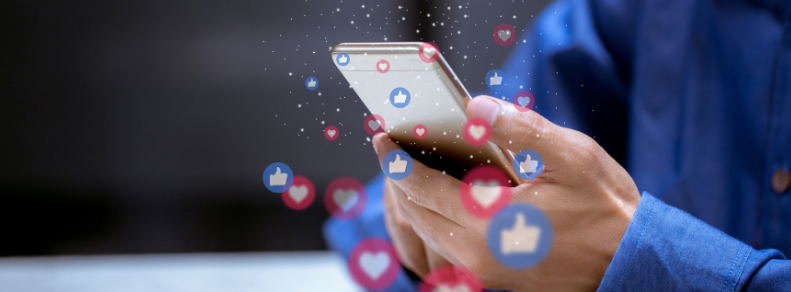 Man holsing a cell phone with Like and Heart emojis scattered surrounding the phone.