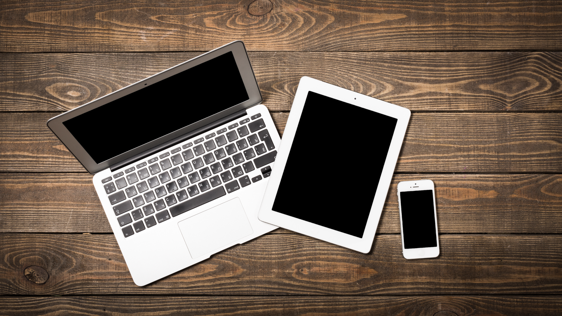 A laptop, tablet and phone on a dark wooden background for a staged branding photo. 