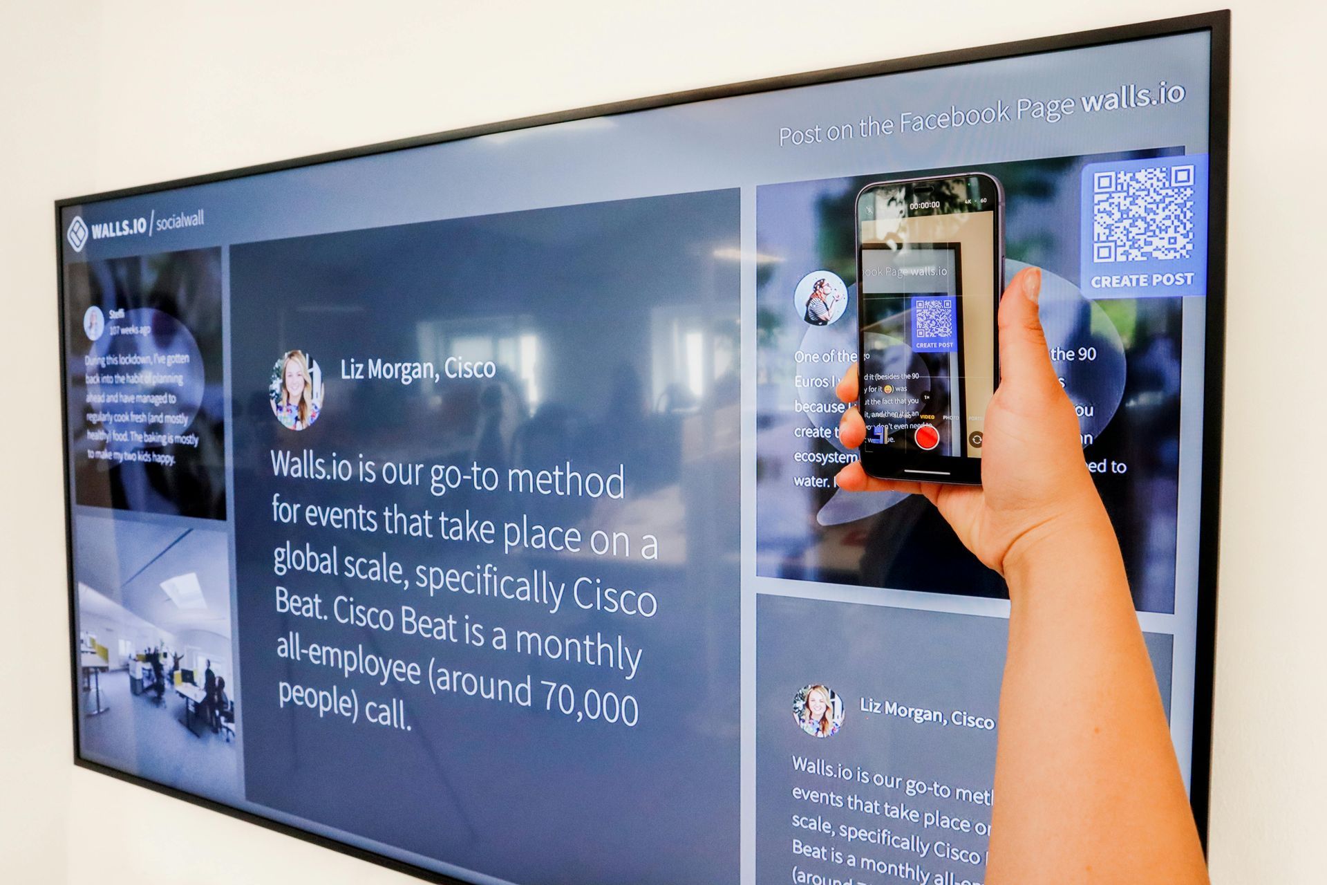 A person holding up a phone in front of a TV, screensharing to the TV, showing social media posts.