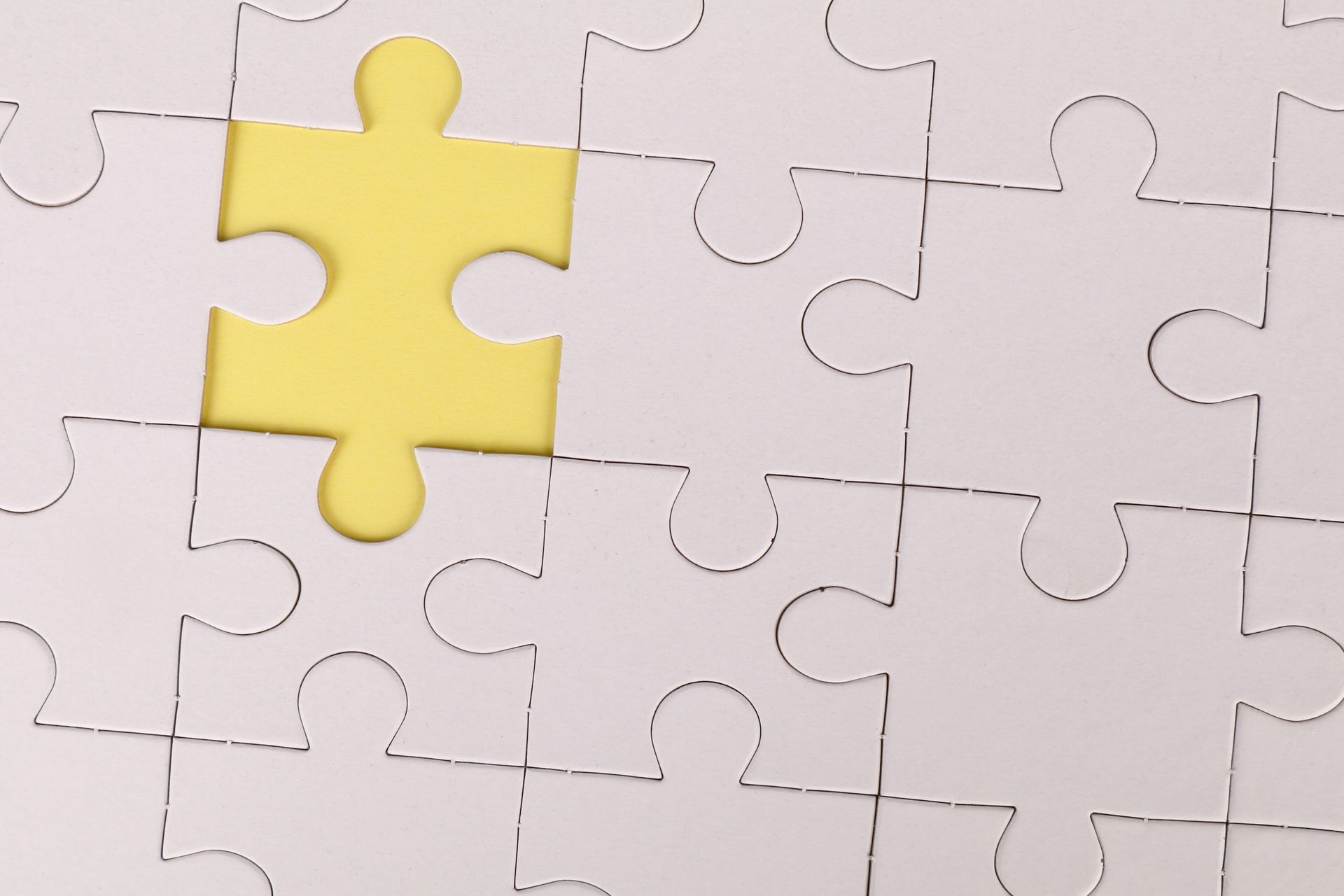 White jigsaw puzzle with one yellow piece missing.