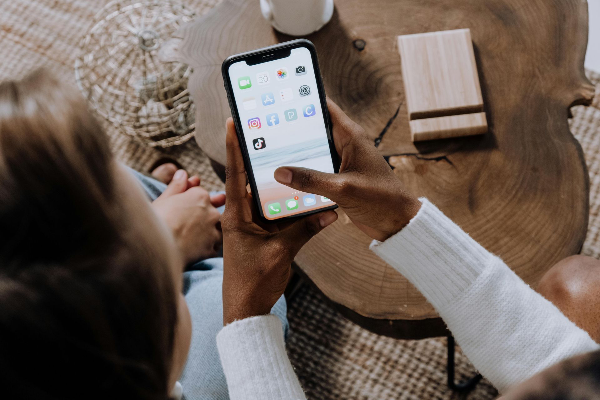 A person is holding a cell phone in front of a wooden table.