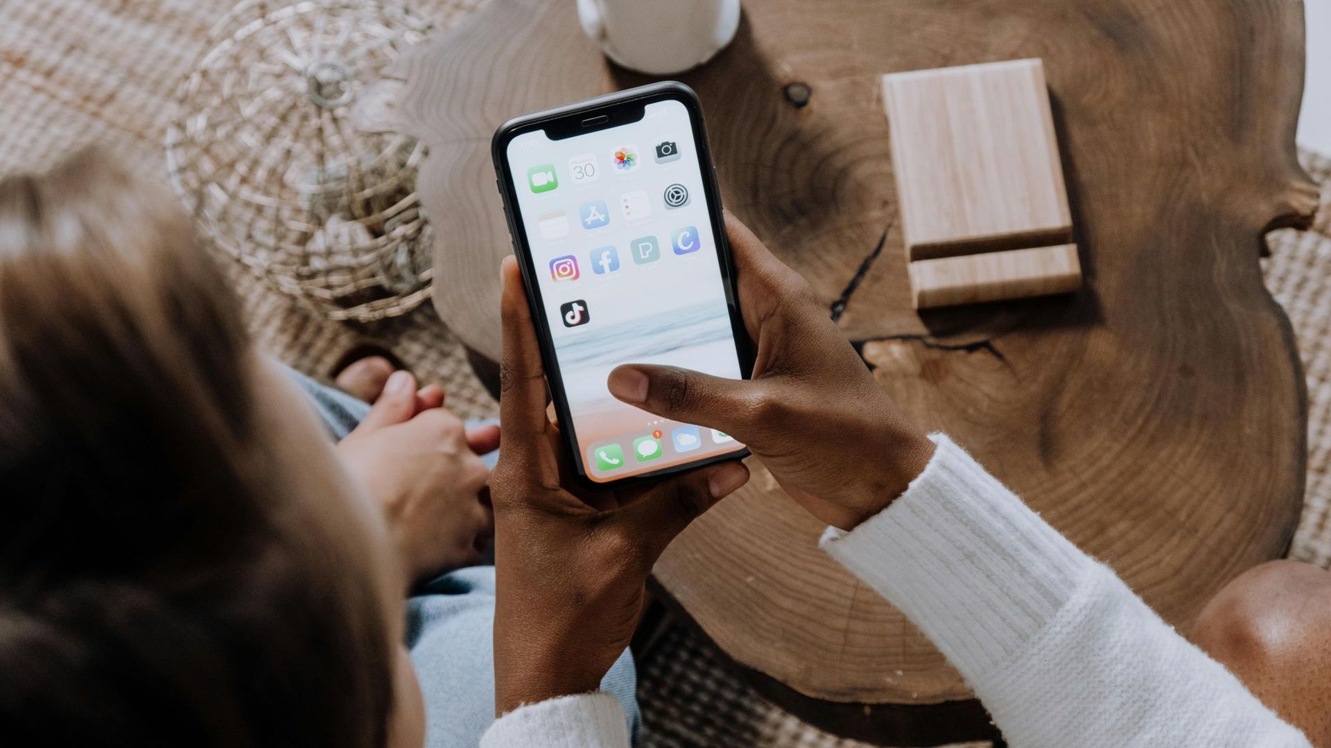 A person is using a cell phone while sitting on a wooden table.
