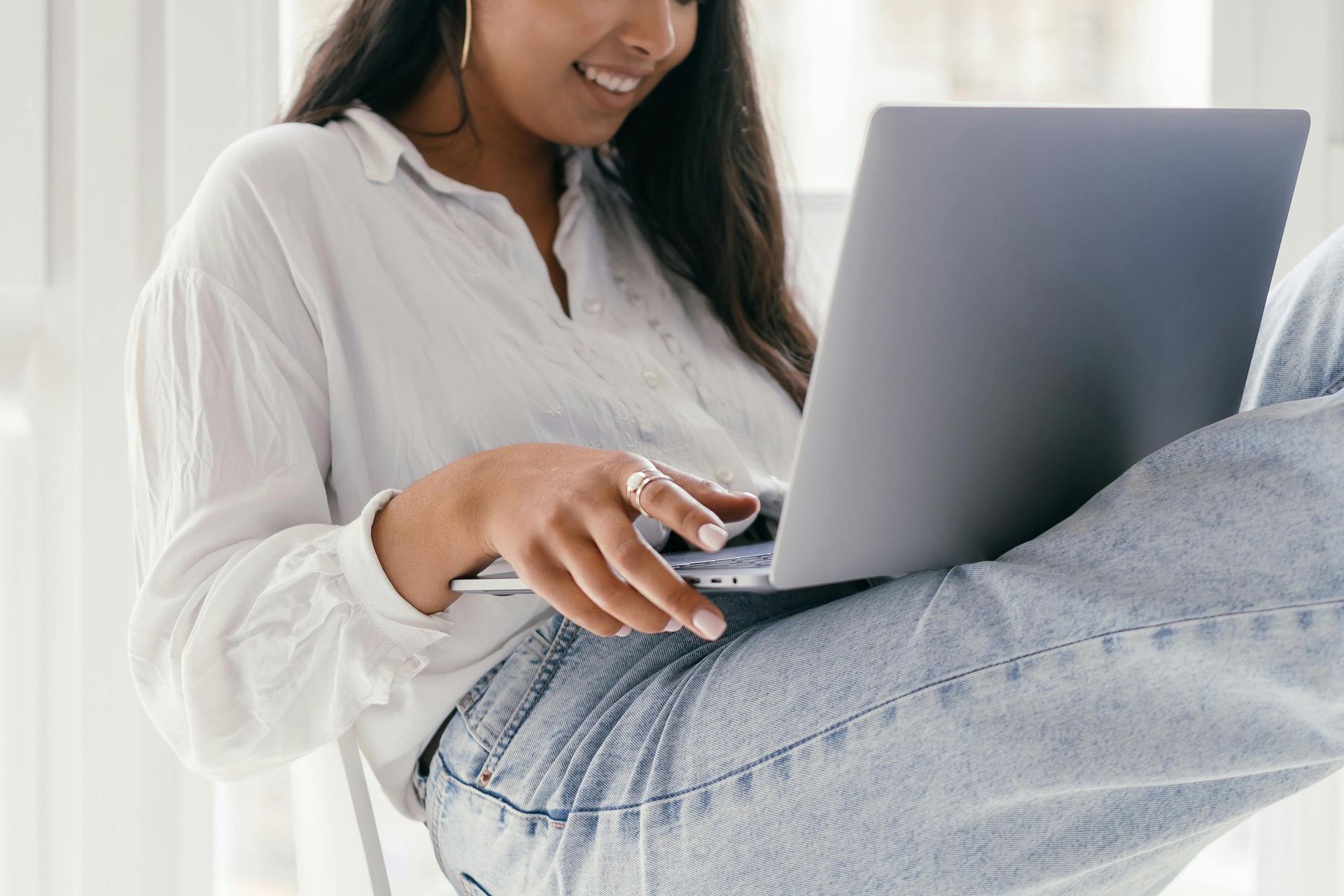 Woman sitting comfortably with a laptop and smiling, representing remote work, digital strategy.