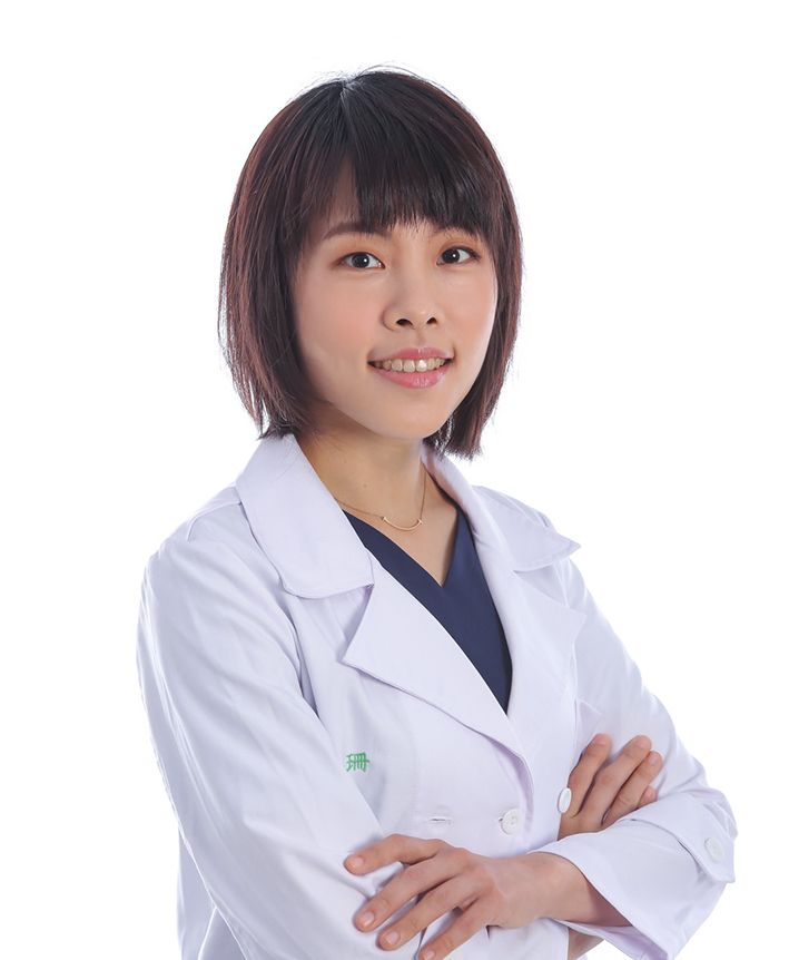 A woman in a white lab coat is sitting down with her hand on her chin.