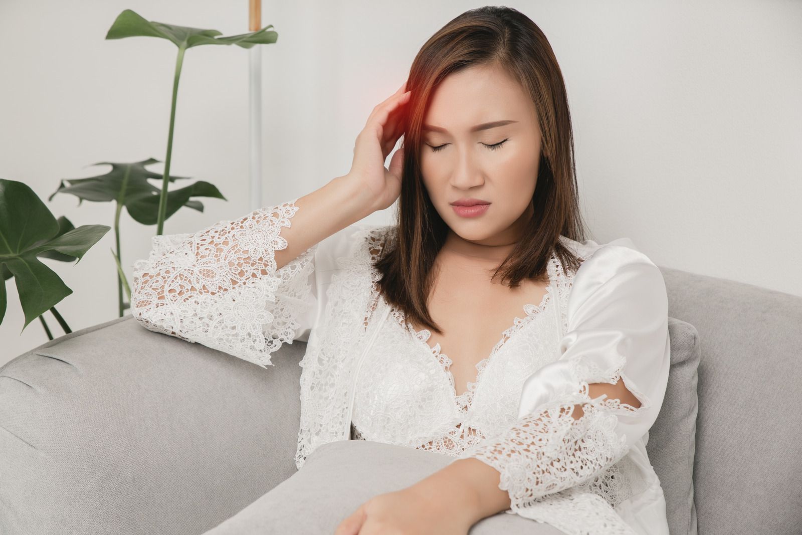 Woman with headache, touching head; sitting on couch. Red highlight indicates pain.