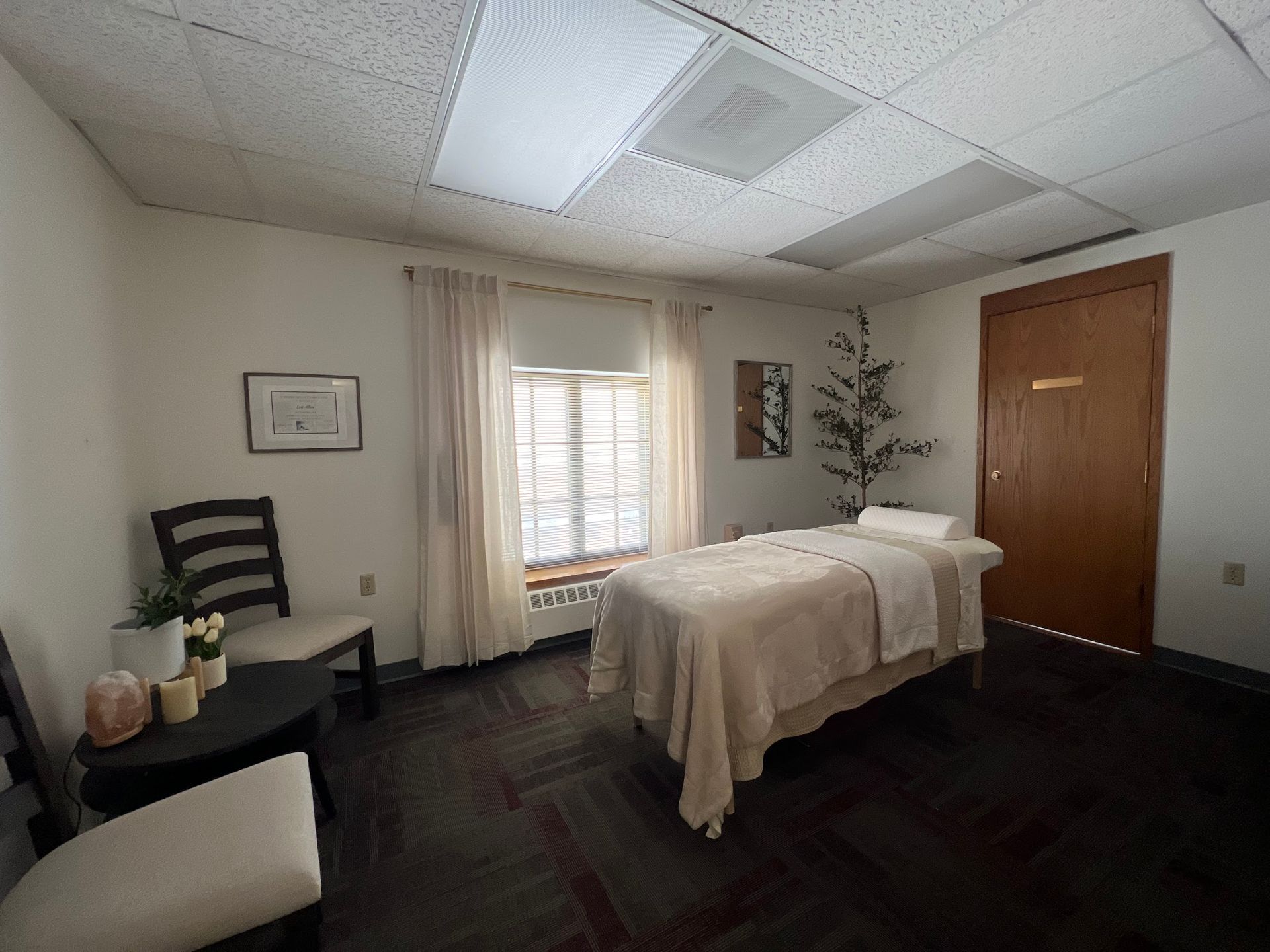 Massage room with a massage table, chairs, and a window.