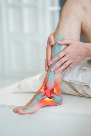 Man holding his ankle, which is highlighted with red and blue to show pain, indoors.