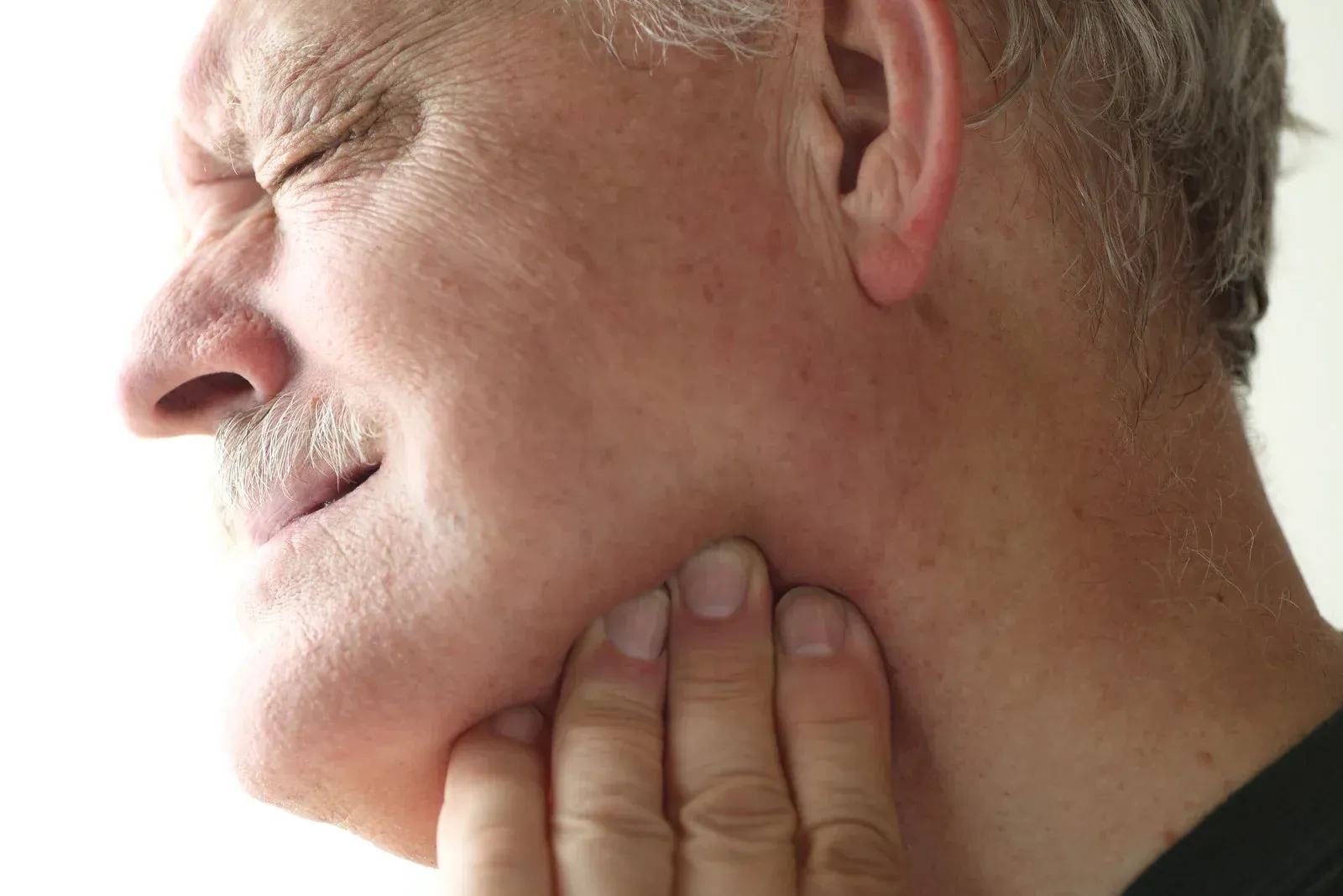 Man with closed eyes, clutching jaw in pain.