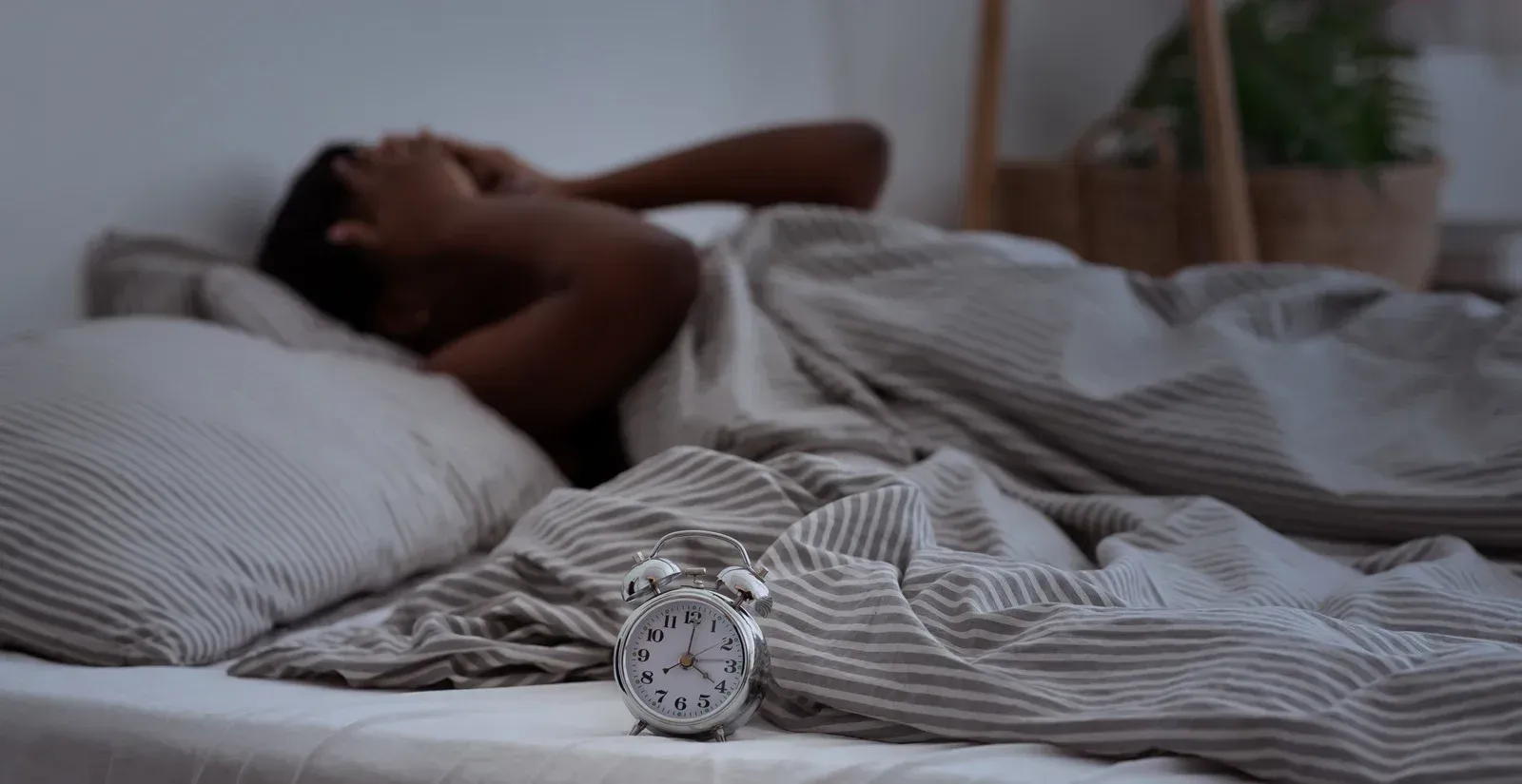 Man in bed, covering ears, alarm clock on the sheets.