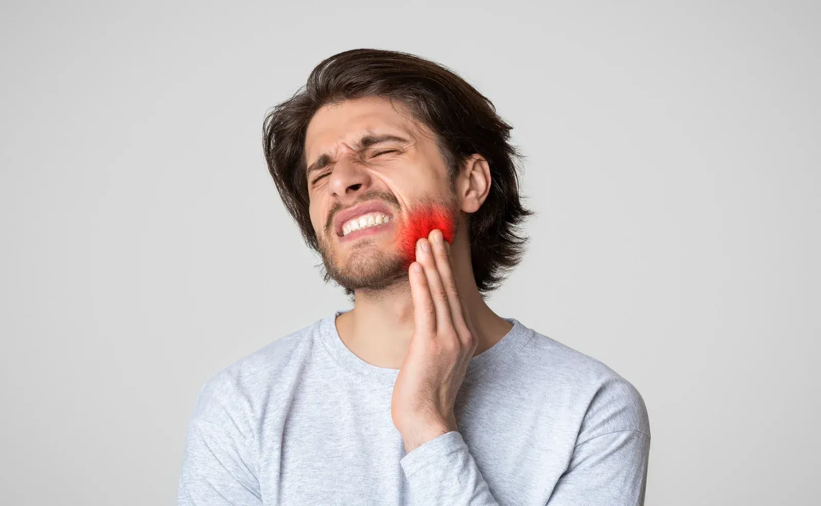 Man with pained expression, holding cheek in pain, red highlight on face indicating pain.