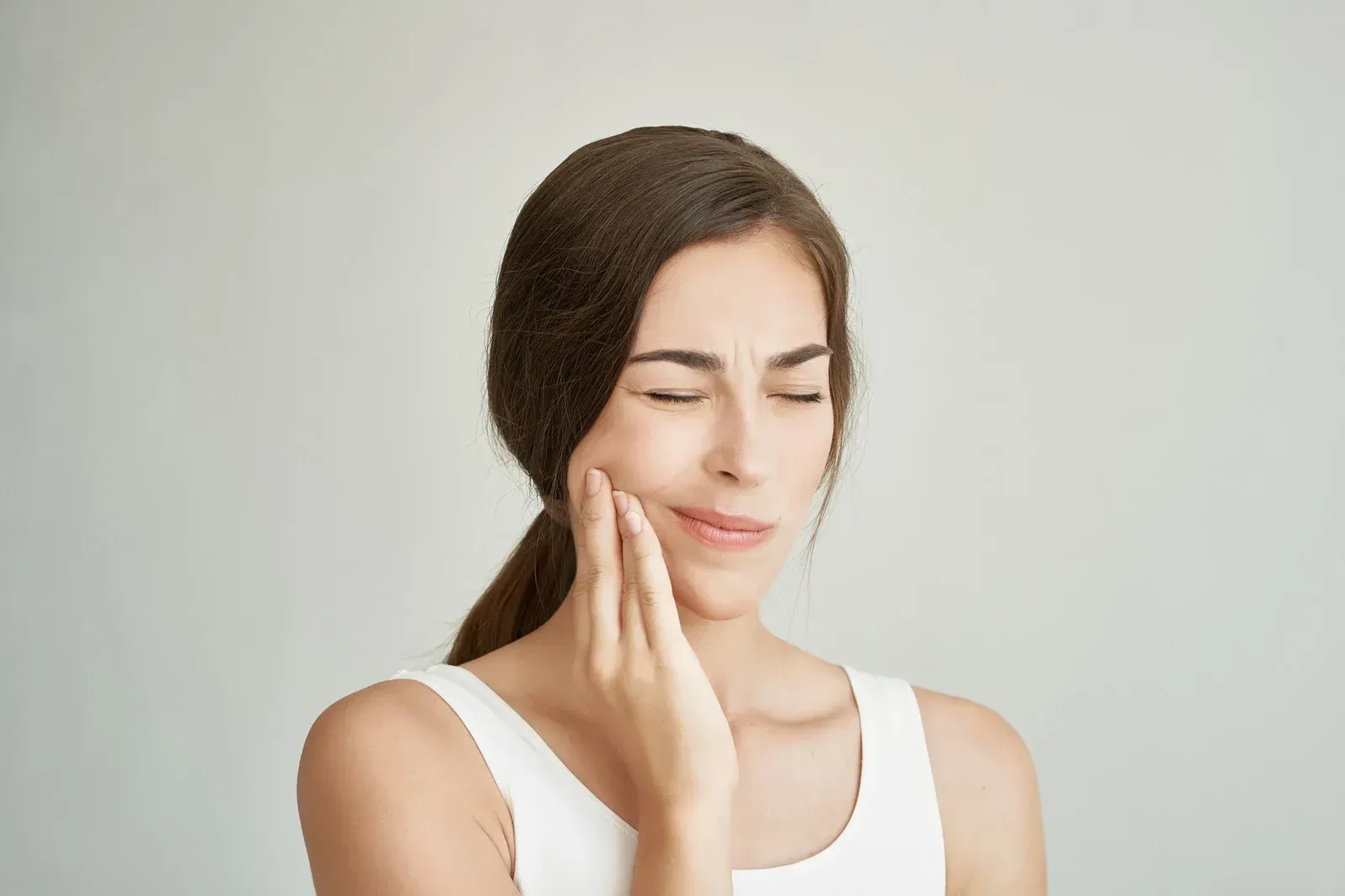 Woman with closed eyes holding her cheek, possibly in pain.