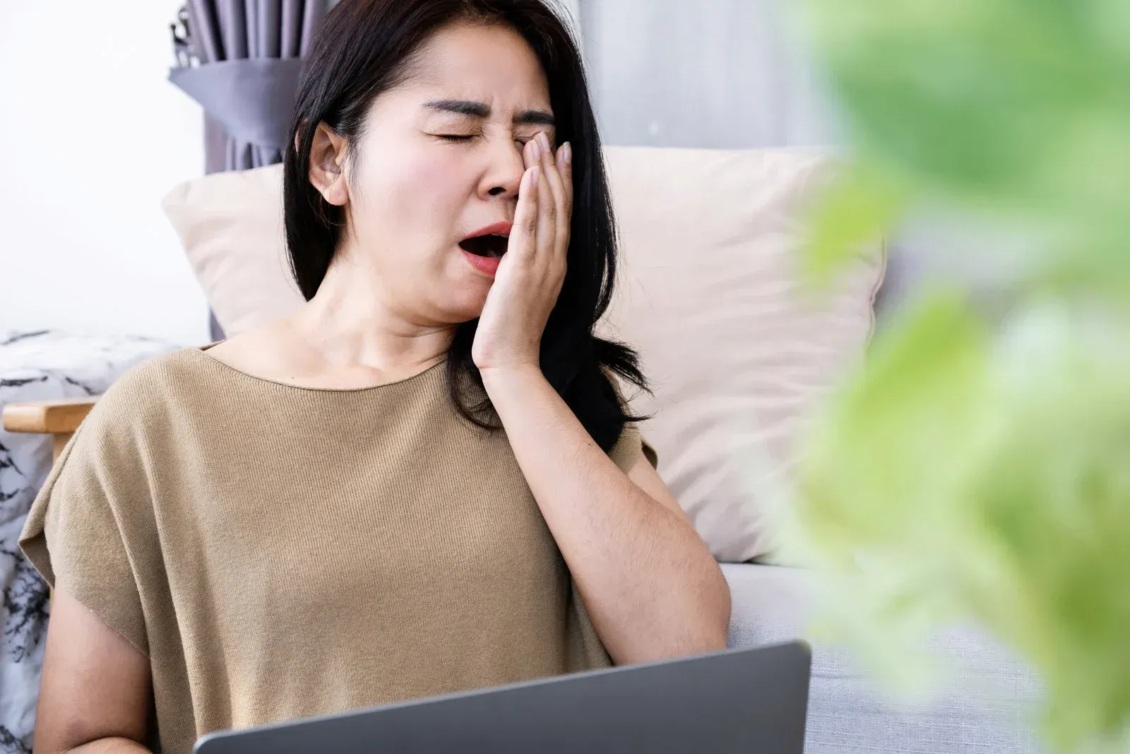 Woman yawning, sitting with laptop, indoors.