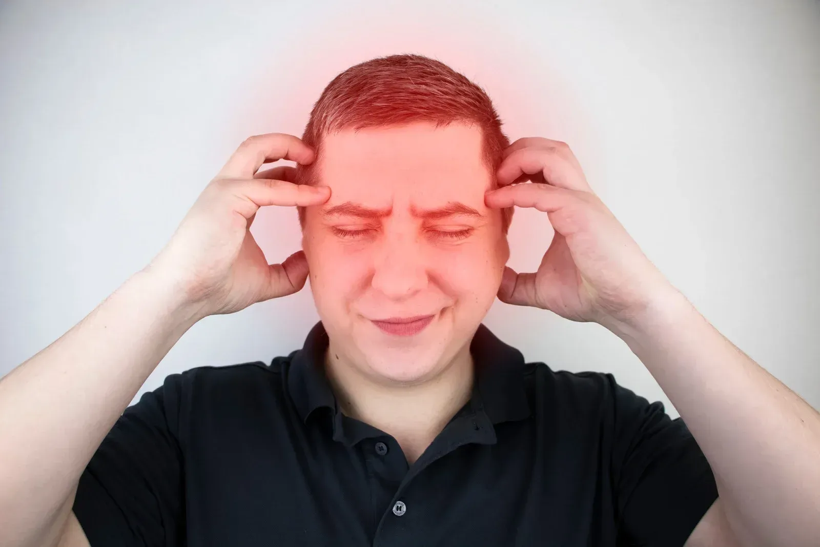 Man with hands on head, red glow highlights head and face, showing pain.