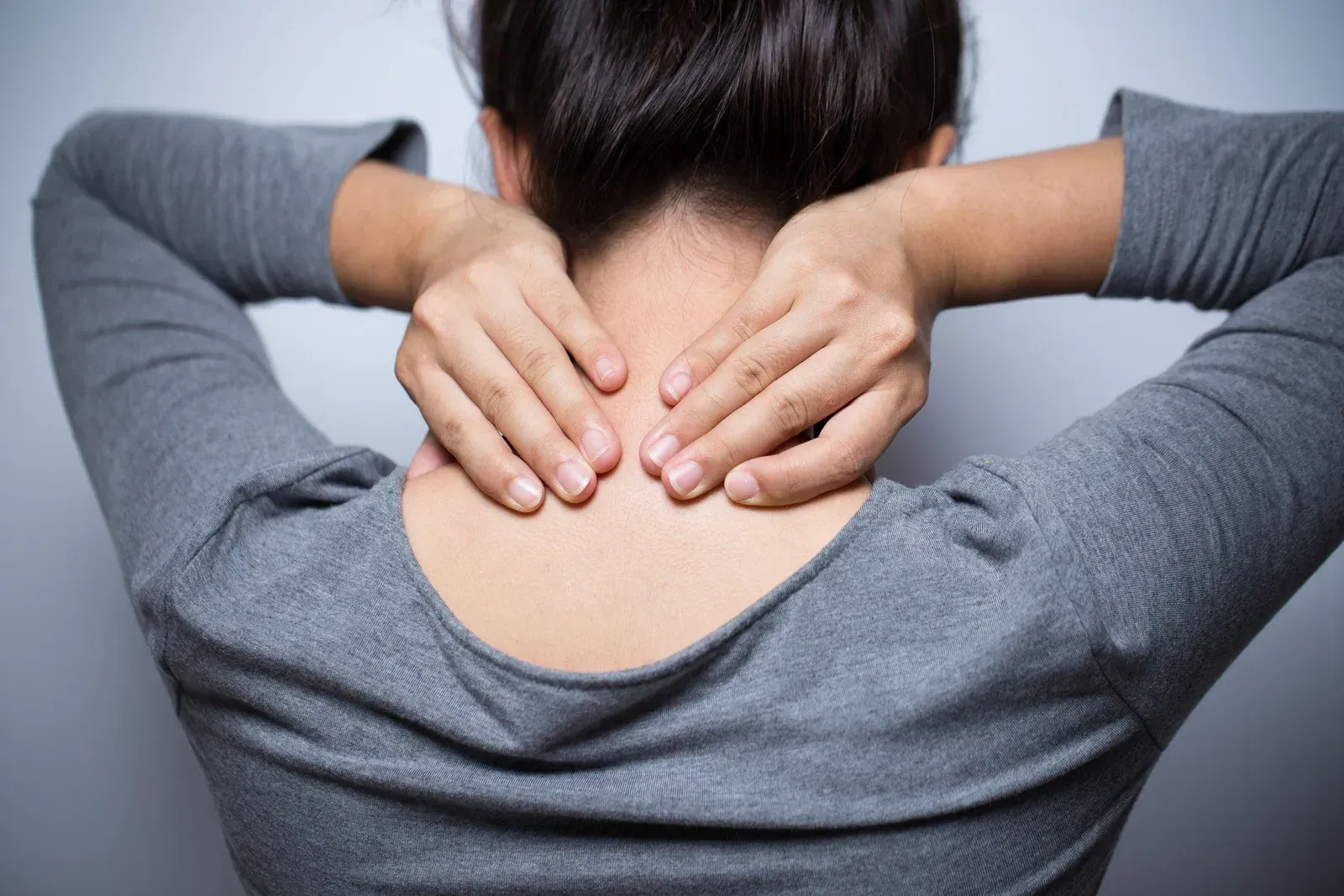 Woman holding her neck in pain, gray shirt, against a white background.