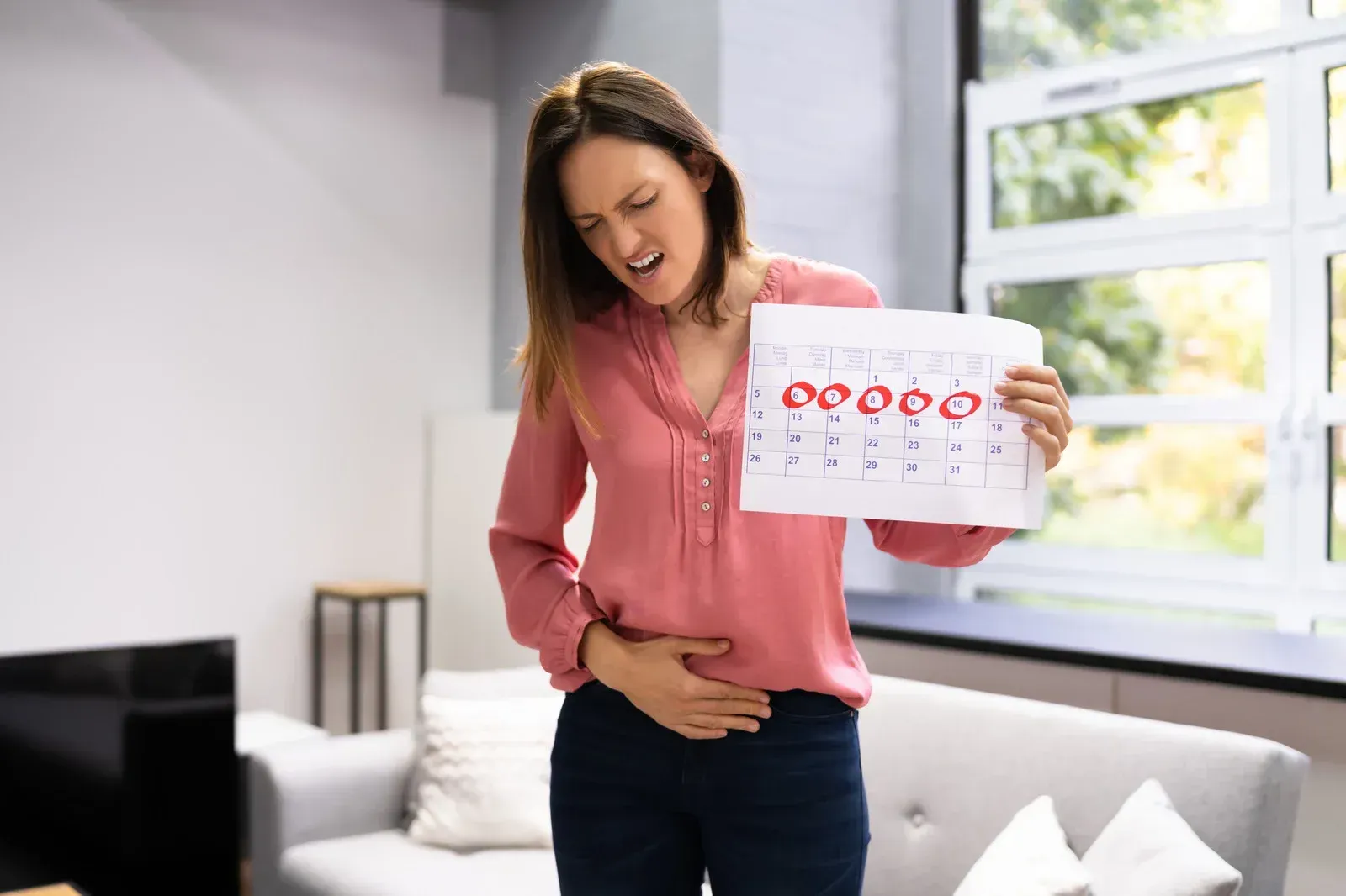 Woman in pain holding calendar marking menstruation, clutching stomach.