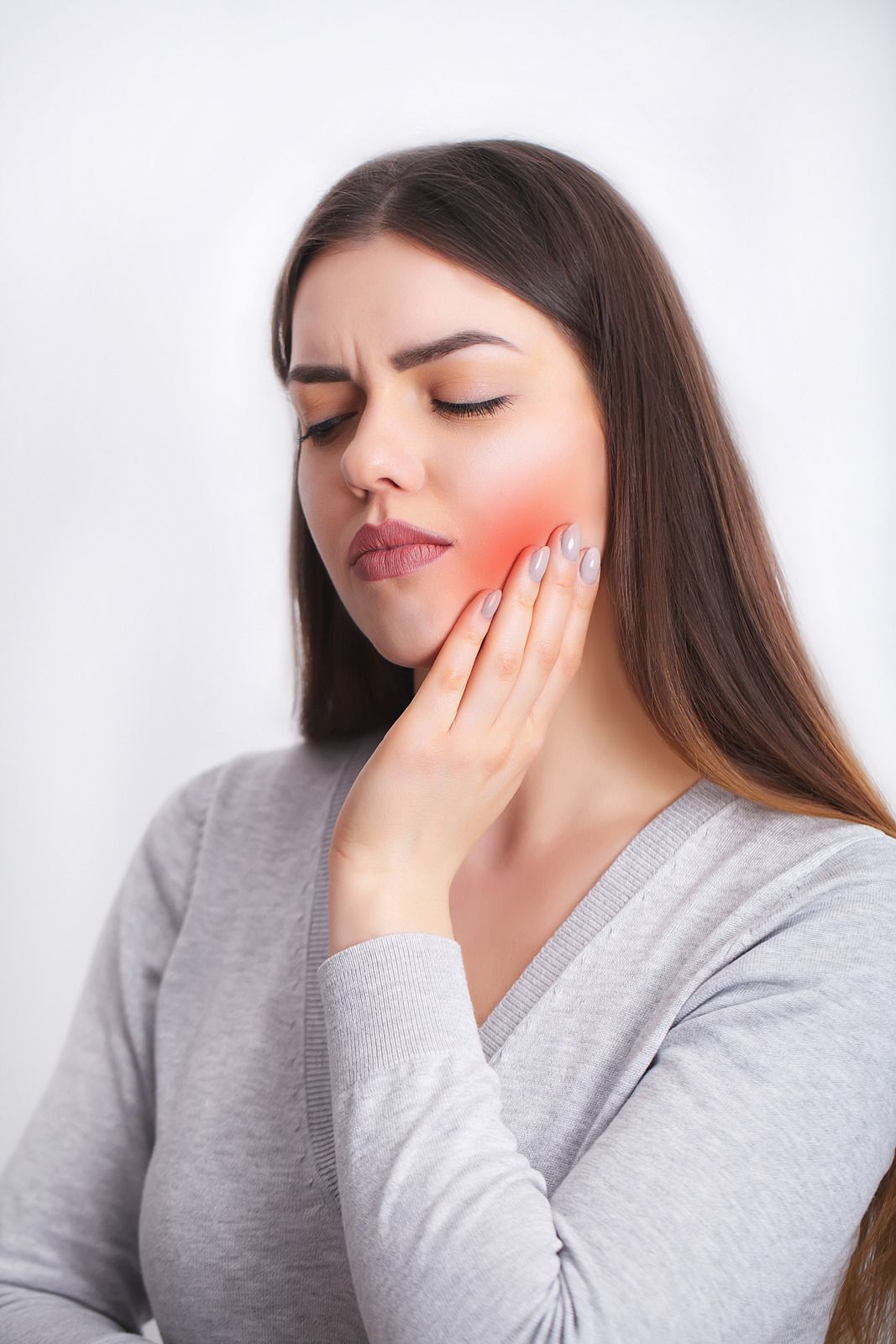 Woman with long brown hair, touching cheek with a red inflamed area; appears to be in pain.
