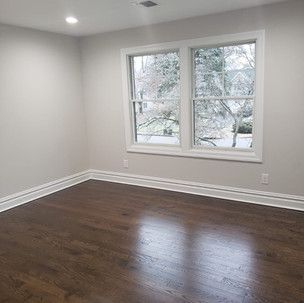 An empty room with hardwood floors and two windows.