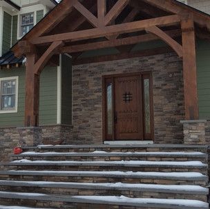 The front of a house with a wooden porch and stairs covered in snow.