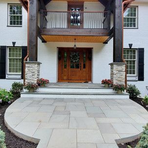 A large white house with a wooden door and a patio in front of it.