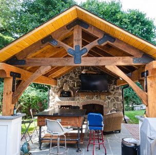 A wooden pavilion with a stone fireplace and a flat screen tv.