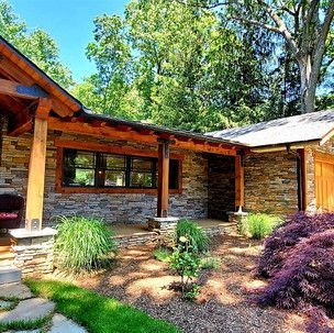 A stone house with a wooden roof and a covered porch surrounded by trees.