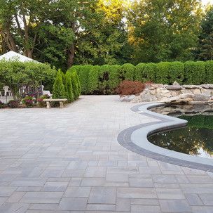 A patio with a pond in the middle of it and trees in the background.