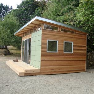 A small wooden house with a green roof is in the middle of a forest.