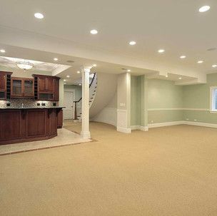 An empty basement with a kitchen , bar , and stairs.