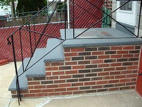 A brick porch with stairs and a metal railing.