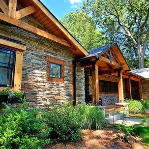 A stone house with a wooden roof and a porch surrounded by trees.