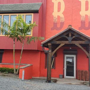A red building with a wooden porch and a tree in front of it.