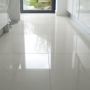 A white tiled floor in a kitchen with a reflection of a window.