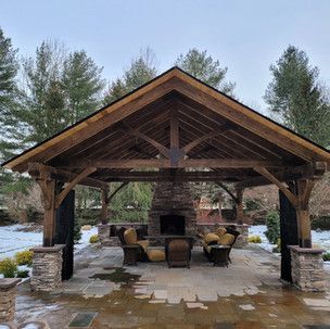 A wooden pavilion with a fireplace and chairs underneath it.